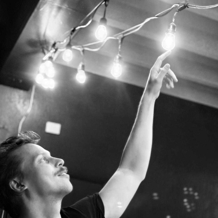 Black-and-white photo of James D. Kent reaching up to touch one of a string of hanging light bulbs